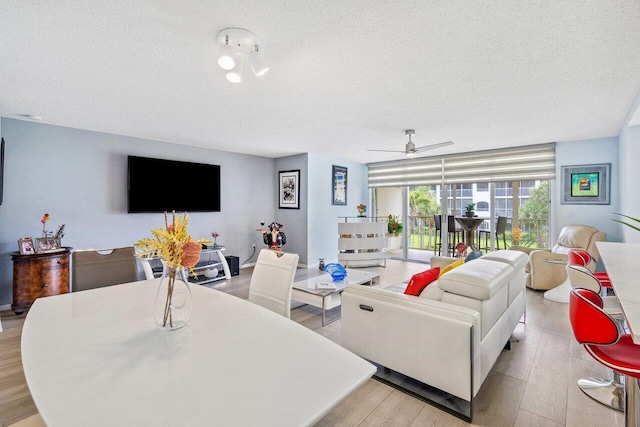 living room with light hardwood / wood-style flooring, ceiling fan, and a textured ceiling