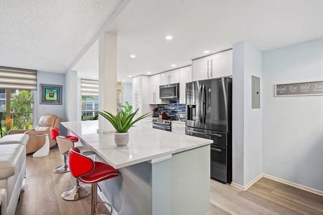 kitchen featuring appliances with stainless steel finishes, a breakfast bar, light hardwood / wood-style floors, and white cabinets