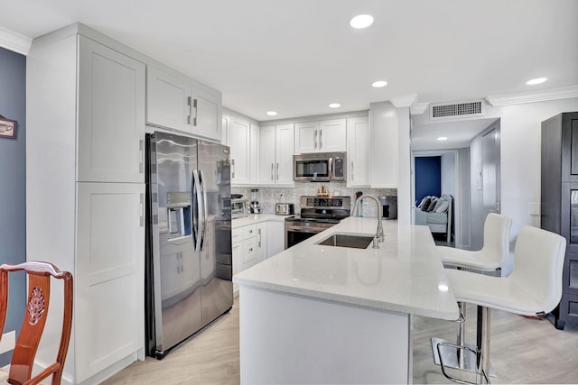 kitchen featuring visible vents, appliances with stainless steel finishes, a sink, a peninsula, and a kitchen breakfast bar