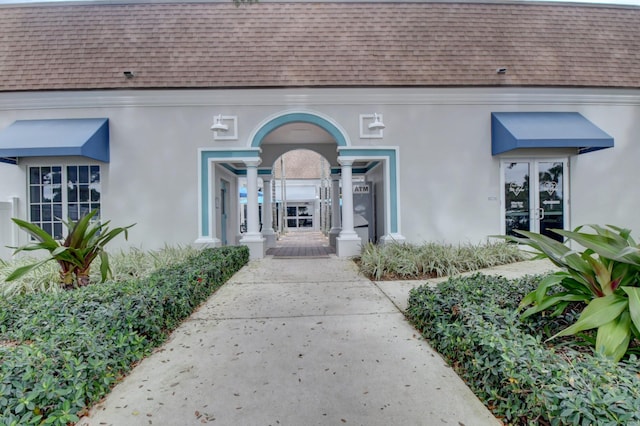 property entrance featuring french doors, roof with shingles, mansard roof, and stucco siding