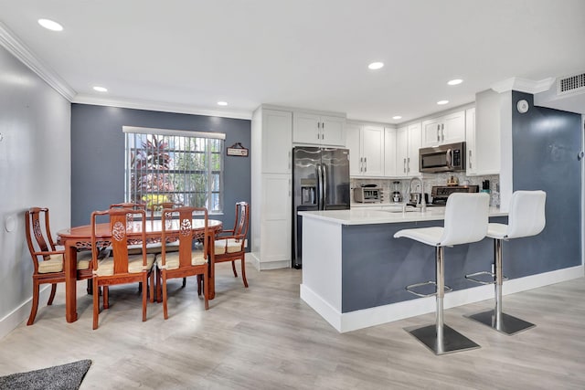 kitchen with a kitchen breakfast bar, light countertops, ornamental molding, appliances with stainless steel finishes, and decorative backsplash