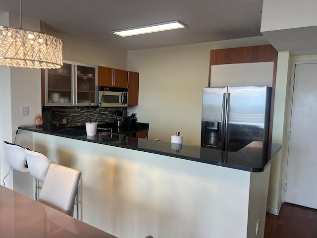 kitchen with appliances with stainless steel finishes, backsplash, hanging light fixtures, kitchen peninsula, and a kitchen breakfast bar