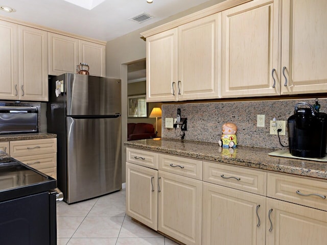 kitchen with stainless steel refrigerator, light tile flooring, backsplash, dark stone counters, and black range with electric cooktop