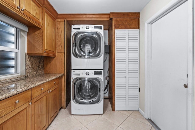 laundry room featuring stacked washer and dryer, light tile patterned floors, and cabinets