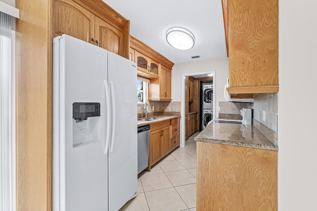 kitchen with backsplash, stacked washer and clothes dryer, light tile patterned floors, stainless steel appliances, and light stone countertops