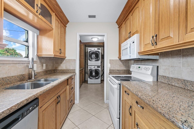 kitchen featuring stacked washer and clothes dryer, sink, light stone counters, light tile patterned floors, and white appliances