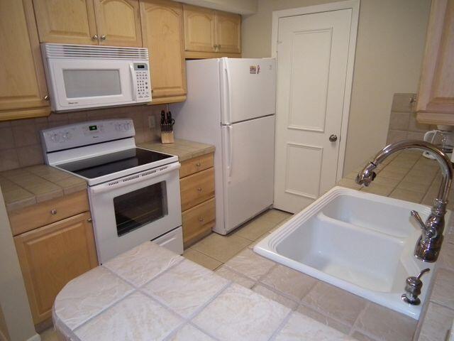 kitchen featuring sink, white appliances, tile counters, and light brown cabinets