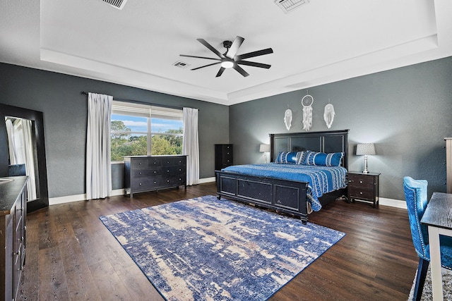 bedroom with dark hardwood / wood-style floors, a tray ceiling, and ceiling fan