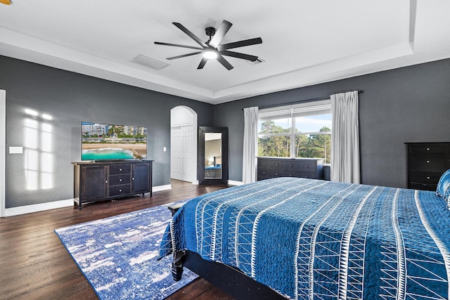 bedroom with dark hardwood / wood-style flooring, a tray ceiling, and ceiling fan