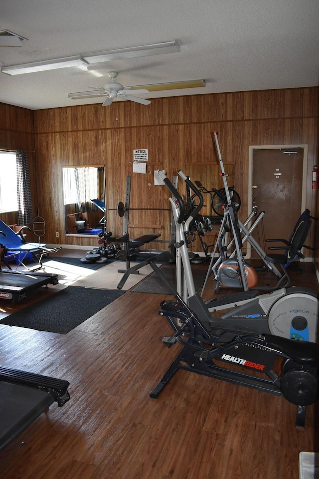 workout room with ceiling fan, wood walls, and wood-type flooring