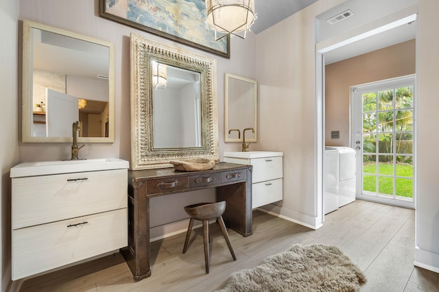 bathroom with dual sinks, washer and dryer, vanity with extensive cabinet space, and hardwood / wood-style floors