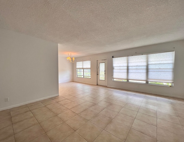 empty room featuring a chandelier, a textured ceiling, and light tile patterned floors