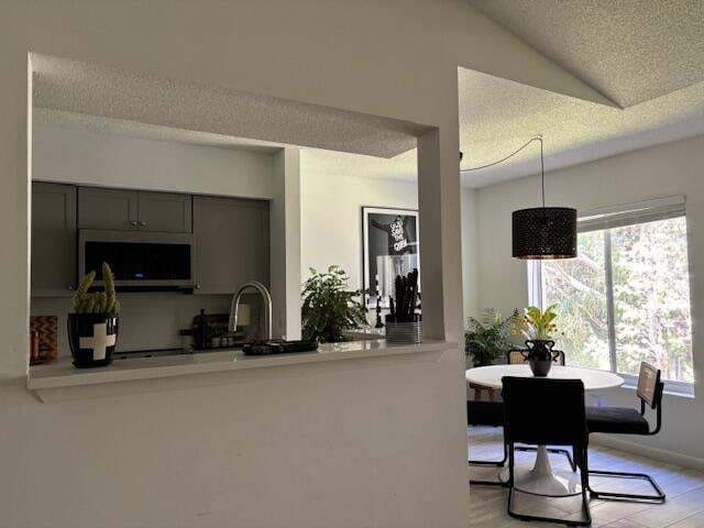 kitchen with lofted ceiling, sink, a textured ceiling, decorative light fixtures, and light hardwood / wood-style flooring