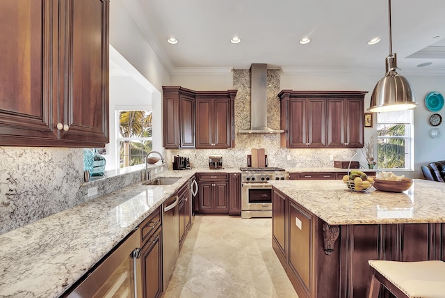 kitchen featuring backsplash, wall chimney range hood, hanging light fixtures, sink, and appliances with stainless steel finishes