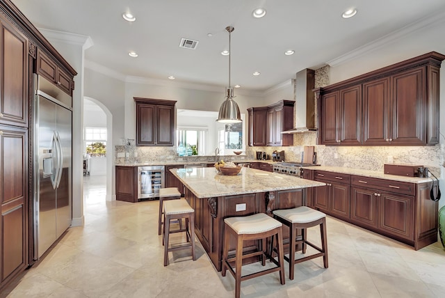 kitchen featuring wall chimney exhaust hood, beverage cooler, stainless steel appliances, a kitchen island, and ornamental molding