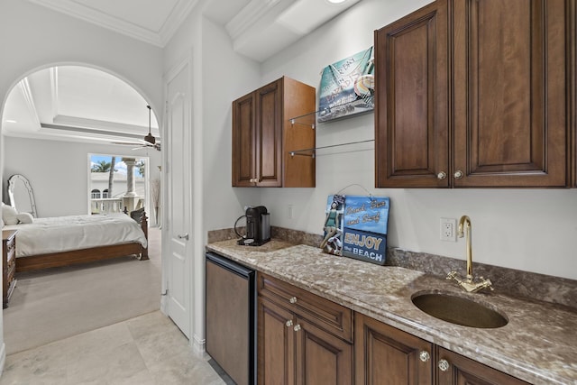 kitchen with stainless steel refrigerator, sink, ornamental molding, ceiling fan, and light stone counters