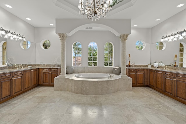 bathroom with ornate columns, vanity, and tiled tub