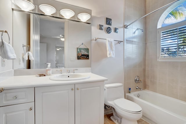 full bathroom with ceiling fan, vanity, tiled shower / bath, and toilet