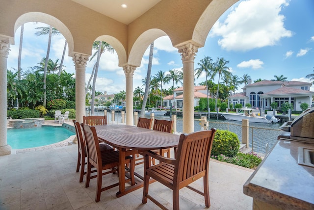 view of patio / terrace featuring a water view, exterior kitchen, and a pool with hot tub