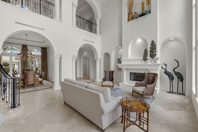 living room featuring a chandelier, a premium fireplace, decorative columns, and a towering ceiling