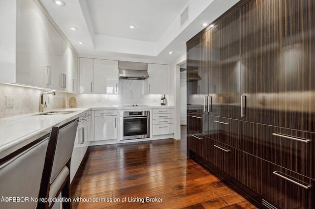 kitchen featuring dark hardwood / wood-style flooring, fume extractor, stainless steel oven, and sink