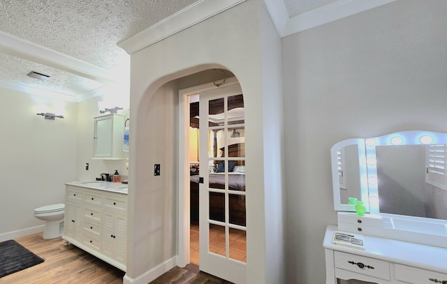 interior space featuring toilet, wood-type flooring, a textured ceiling, and ornamental molding