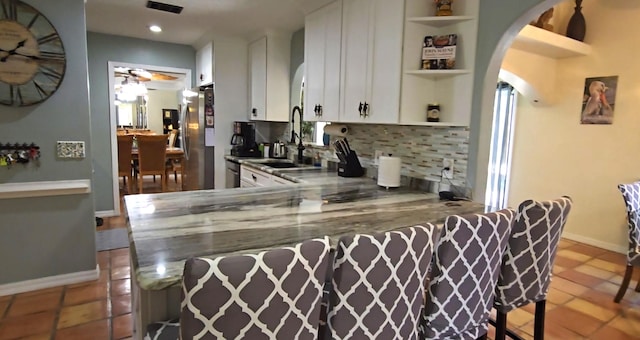 kitchen featuring sink, tasteful backsplash, kitchen peninsula, stainless steel fridge, and white cabinets