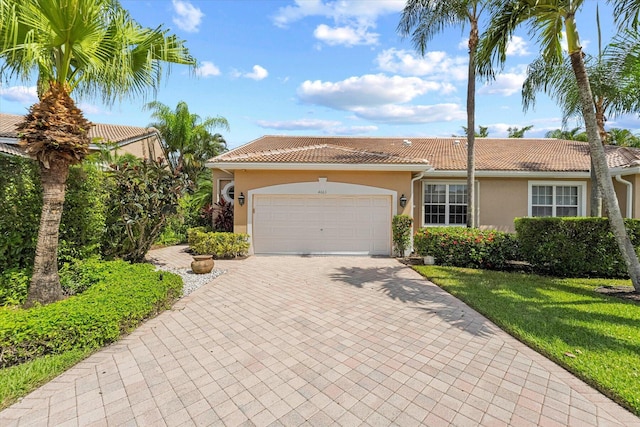 view of front facade with a tiled roof, stucco siding, decorative driveway, a front yard, and an attached garage