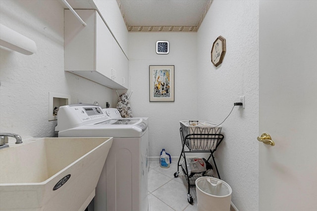 clothes washing area with a textured wall, light tile patterned floors, independent washer and dryer, cabinet space, and a sink