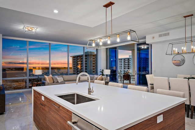 kitchen featuring an island with sink, sink, a wall of windows, dishwasher, and pendant lighting