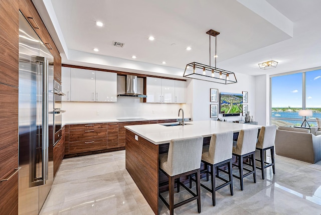 kitchen featuring sink, white cabinets, a kitchen island with sink, and wall chimney exhaust hood