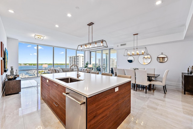 kitchen featuring hanging light fixtures, stainless steel dishwasher, a wall of windows, sink, and a kitchen island with sink