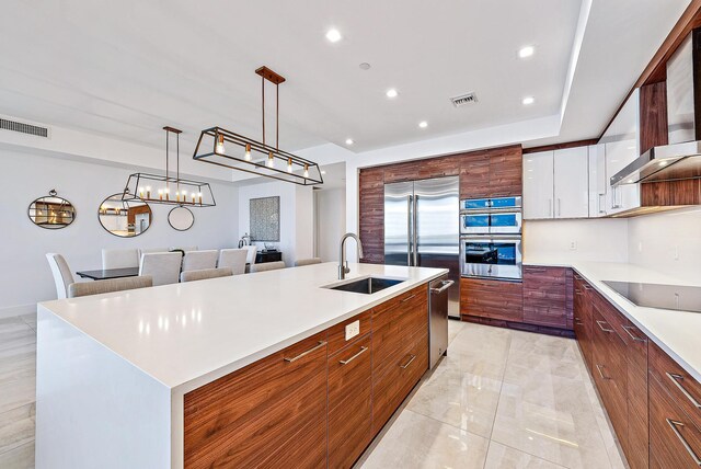 kitchen with a center island with sink, sink, white cabinetry, decorative light fixtures, and stainless steel appliances