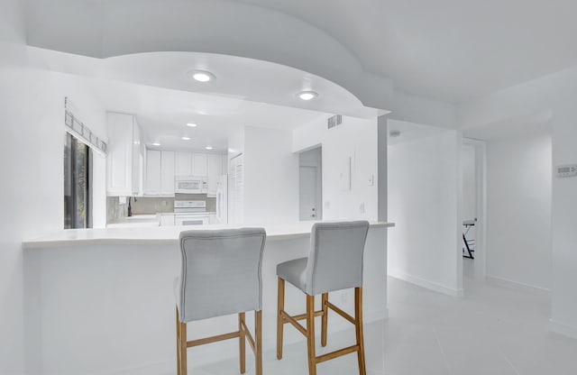 kitchen featuring white cabinets, range, backsplash, kitchen peninsula, and light tile floors