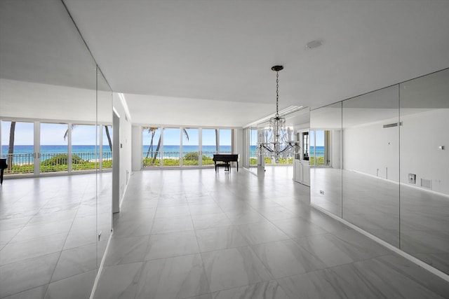 spare room featuring a water view, an inviting chandelier, and floor to ceiling windows