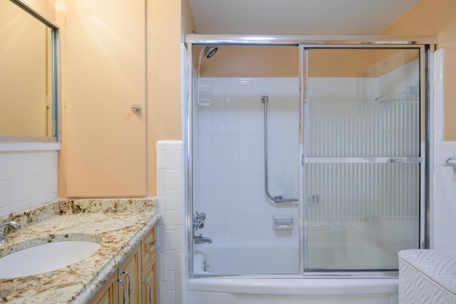 bathroom featuring tile walls, large vanity, and bath / shower combo with glass door