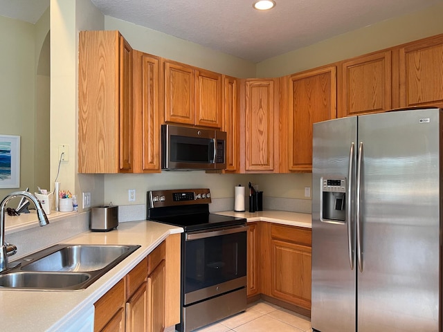 kitchen with light tile patterned flooring, appliances with stainless steel finishes, sink, and a textured ceiling