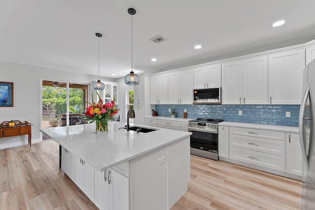 kitchen featuring sink, appliances with stainless steel finishes, an island with sink, pendant lighting, and white cabinets