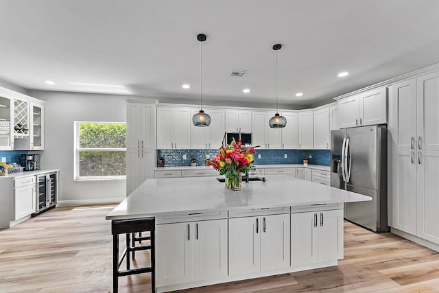 kitchen with white cabinets, hanging light fixtures, a center island, stainless steel refrigerator with ice dispenser, and light hardwood / wood-style flooring