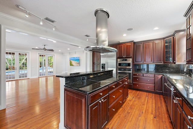 kitchen with a kitchen island, appliances with stainless steel finishes, a textured ceiling, sink, and light hardwood / wood-style flooring