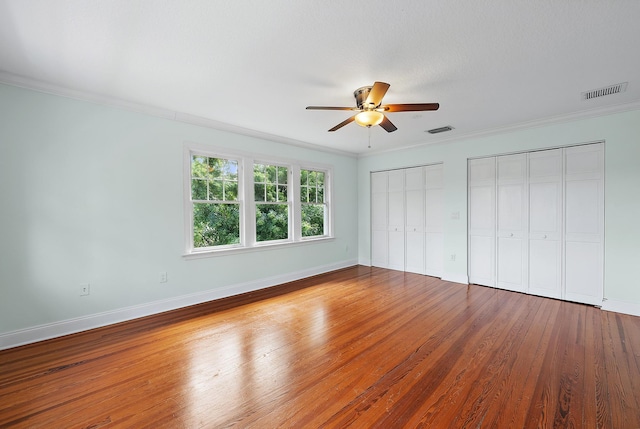 unfurnished bedroom featuring hardwood / wood-style flooring, ceiling fan, crown molding, and two closets