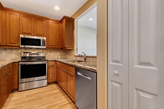 kitchen with tasteful backsplash, light hardwood / wood-style floors, sink, appliances with stainless steel finishes, and light stone counters