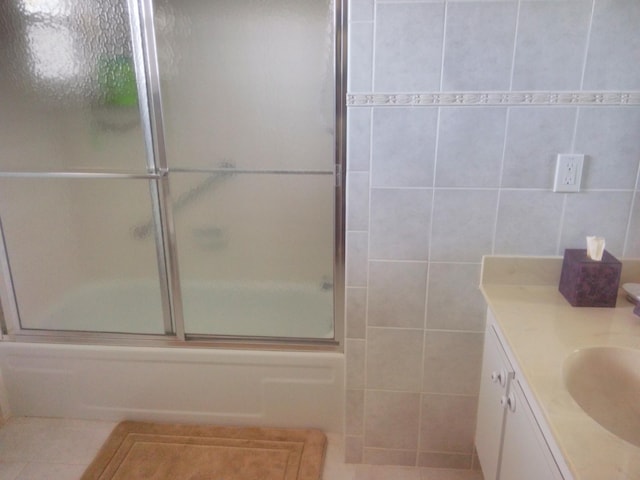 bathroom featuring tile patterned flooring, bath / shower combo with glass door, tile walls, and vanity