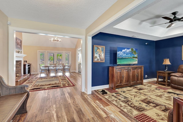 living room featuring hardwood / wood-style floors, a textured ceiling, a fireplace, and ceiling fan with notable chandelier