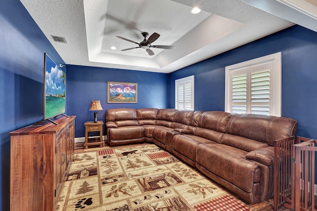 living room featuring hardwood / wood-style floors, a textured ceiling, ceiling fan, and a raised ceiling