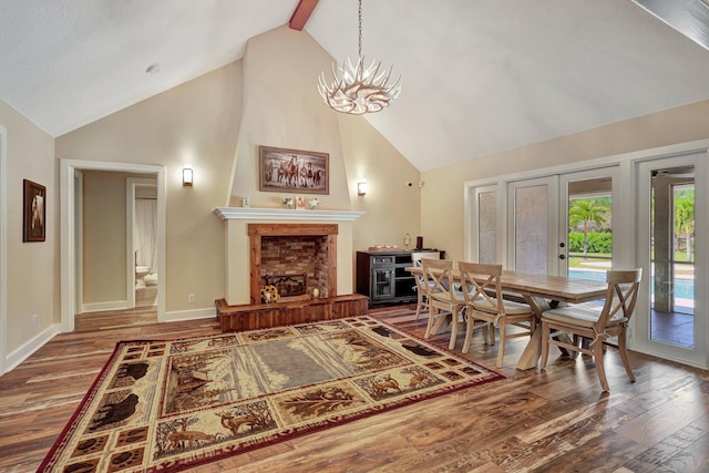 dining room with an inviting chandelier, a brick fireplace, high vaulted ceiling, wood-type flooring, and beamed ceiling