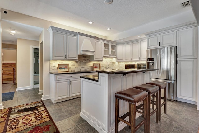 kitchen with dark tile flooring, stainless steel refrigerator with ice dispenser, custom exhaust hood, and backsplash