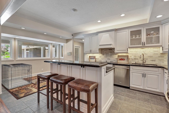 kitchen featuring tasteful backsplash, stainless steel dishwasher, custom range hood, light tile floors, and a center island