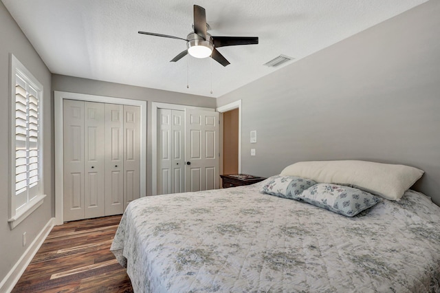 bedroom featuring multiple closets, ceiling fan, a textured ceiling, and dark hardwood / wood-style flooring