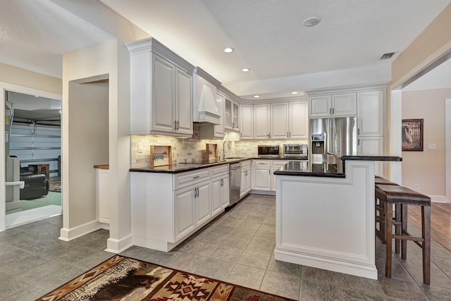 kitchen with stainless steel appliances, premium range hood, backsplash, a breakfast bar area, and white cabinetry